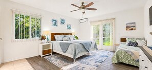 A bedroom with a bed, bedside tables, a ceiling fan, and artwork on the walls.