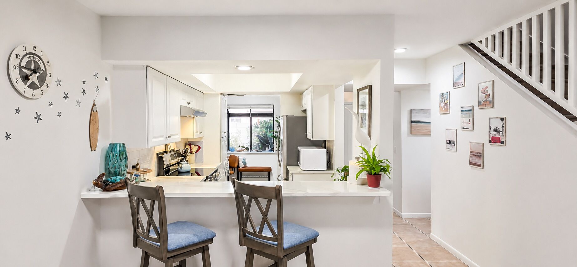 Une cuisine moderne avec un îlot central, deux chaises, une horloge et un escalier menant à un autre niveau.
