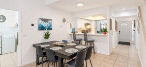 A dining area with a table set for four, chairs, a clock, and a wall-mounted artwork.