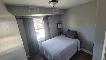 A small, well-lit bedroom with a single bed, a nightstand, and a window with curtains.