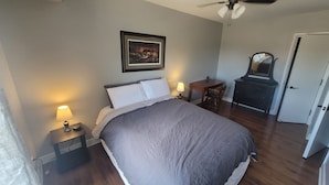 A bedroom with a bed, two bedside lamps, a framed picture on the wall, a dresser, and a door.
