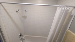 A shower with a white curtain, a chrome showerhead, and a white bathtub.