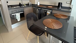 A modern kitchen with wooden cabinets, a black countertop, and a dining area with two black chairs and a round table. - Collection R 5 MONEDA 2 Presidencial  (Santiago)