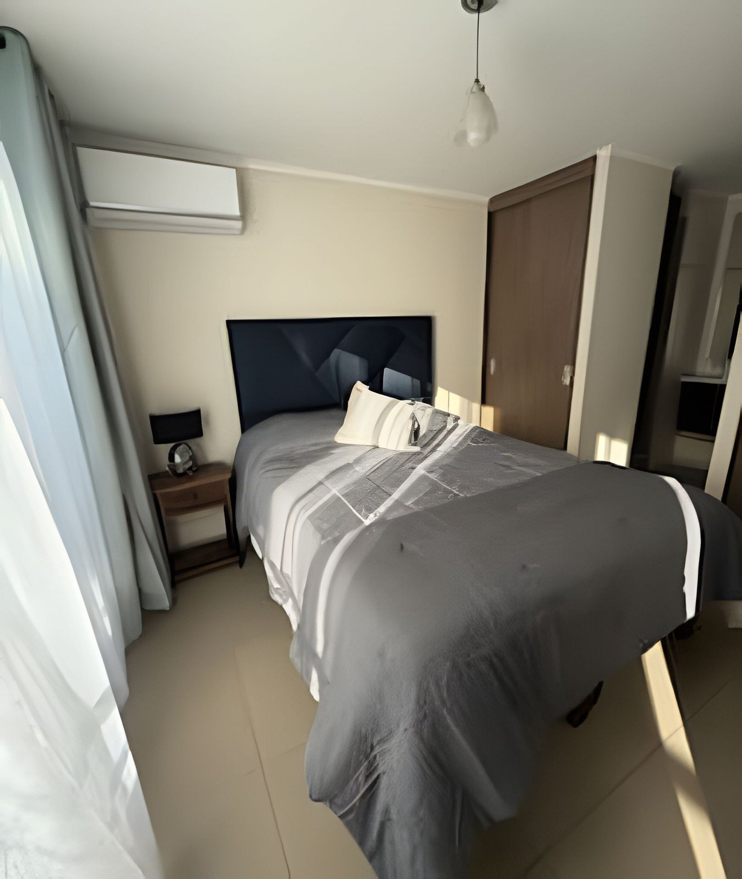 A bedroom with a bed, a nightstand, a lamp, a hanging light fixture, and a door.