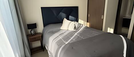 A bedroom with a bed, a nightstand, a lamp, a hanging light fixture, and a door.