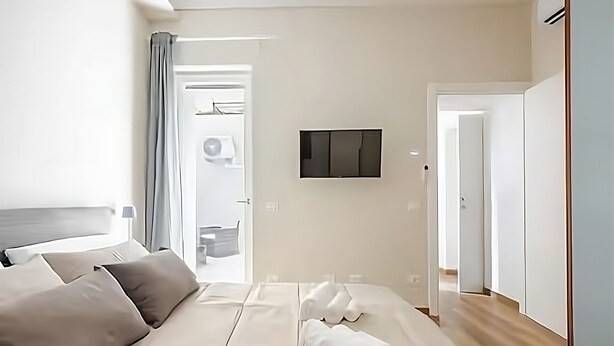 A modern hotel room with a bed, a flat-screen TV mounted on the wall, and a door leading to a bathroom. - Suite 53 Campofiore - with outdoor patio (Verona)