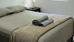 Un dormitorio con una cama, una mesita de noche, una lámpara y una ventana con persiana.