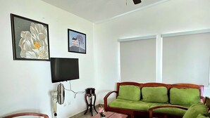 Una sala de estar con ventilador de techo, mobiliario tapizado en tono verde, televisor de pantalla plana y cuadros en la pared.