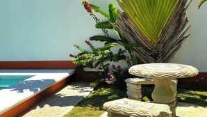 Un jardín con piscina, bancos de piedra y hojas de plátano grandes.