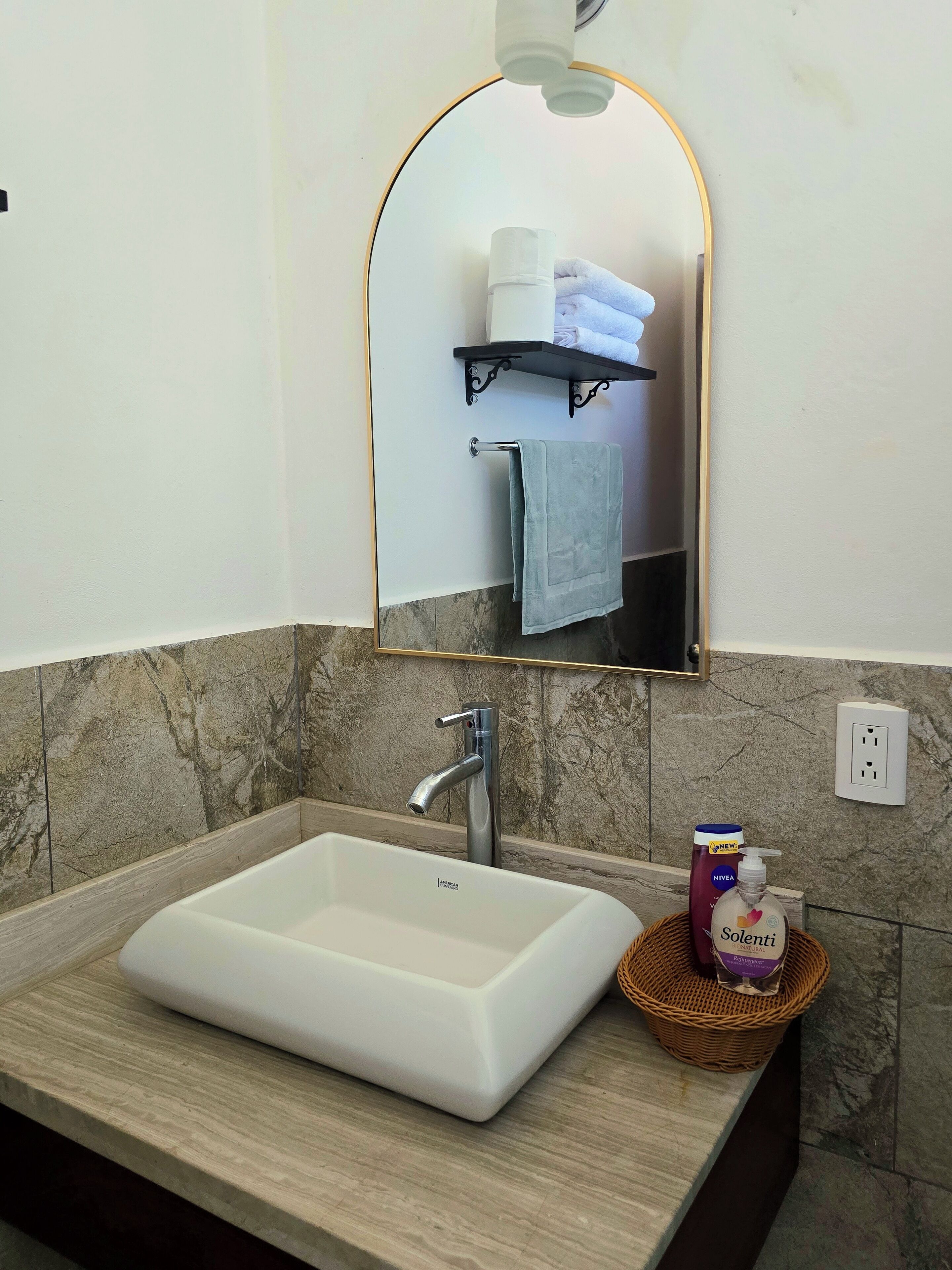 Un bagno con un lavandino bianco, uno specchio a mensola con arco e un portaservizi con asciugamani.