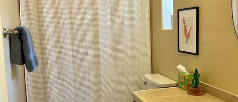 Ein Badezimmer mit Duschvorhang, Toilette, Waschbecken und gerahmten Bildern an der Wand.