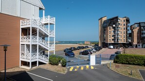 Un edificio costero con una escalera blanca, un estacionamiento con automóviles y vistas al mar.