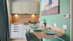 Cocina moderna con armarios blancos, encimera de madera y zona de comedor con pared verde y un cuadro con motivos playeros.