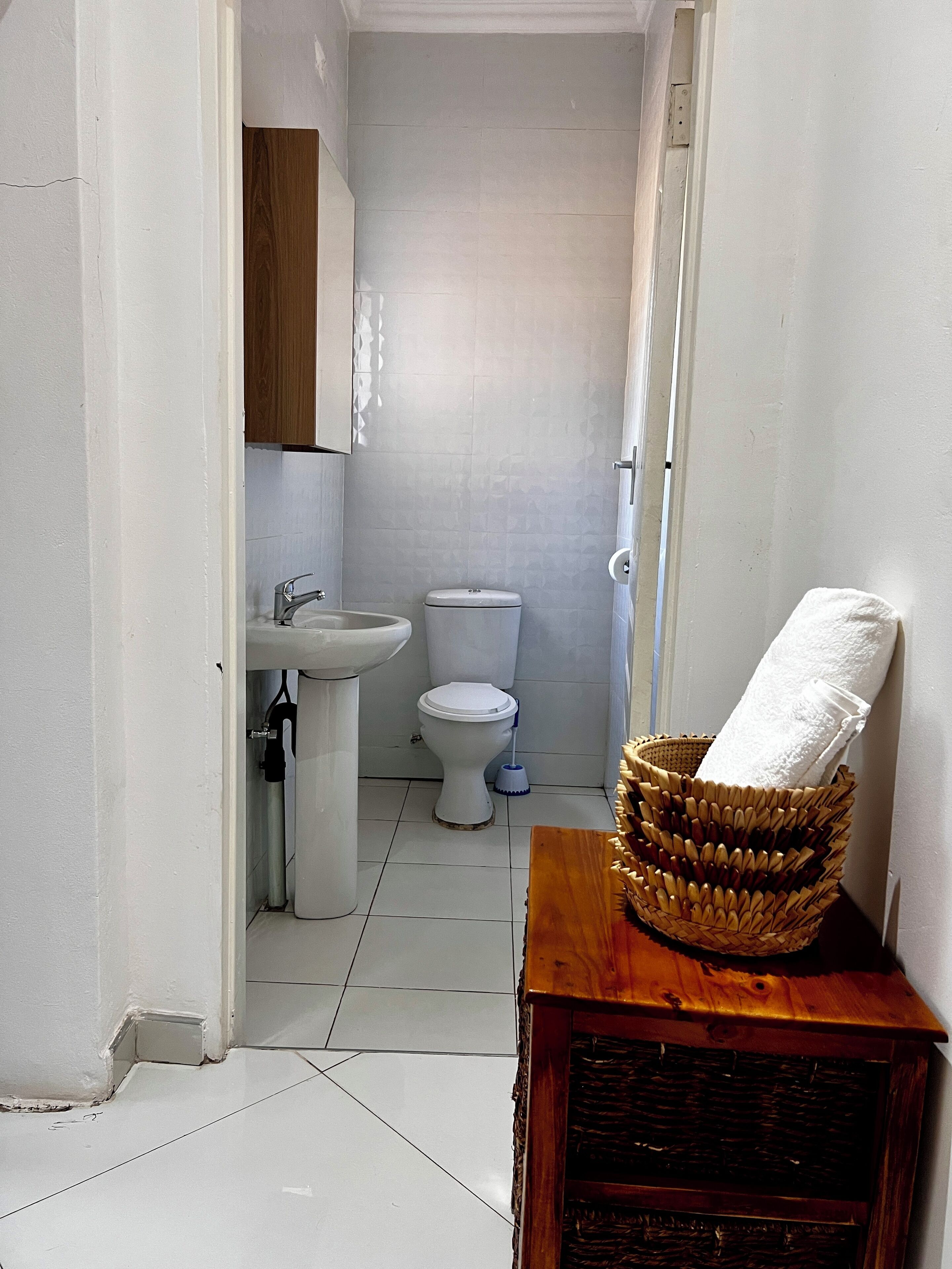 A narrow bathroom with a white toilet, a sink, and a wooden cabinet.
