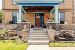 Un bâtiment à deux étages avec une façade en briques, un porche en bois doté de colonnes, une porte d’entrée et des marches menant à l’entrée.