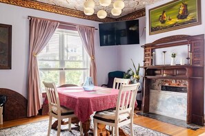 Ein Esszimmer mit Tisch für vier Personen, Kamin und großem Fenster mit Vorhängen.