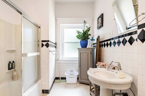Un bagno con doccia, lavandino, una pianta in vaso, una finestra e un armadietto.