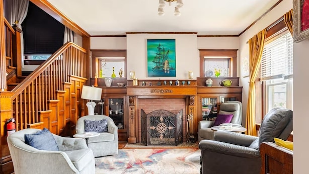 A spacious living room with a fireplace, a staircase, and a large painting above it.