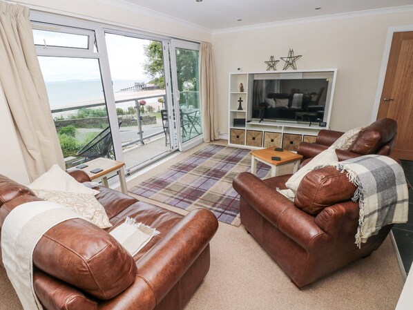 A living room with two brown leather sofas, a coffee table, and a TV stand with decorative items. - Lifeboat Lookout (Tenby)