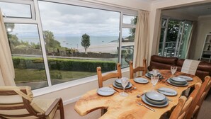 Un comedor con vista al mar, una mesa de madera dispuesta con platos y vasos, y sillas de cuero.