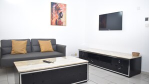 Een moderne woonkamer met een grijze bank, een salontafel, een televisie en een kast met lades.