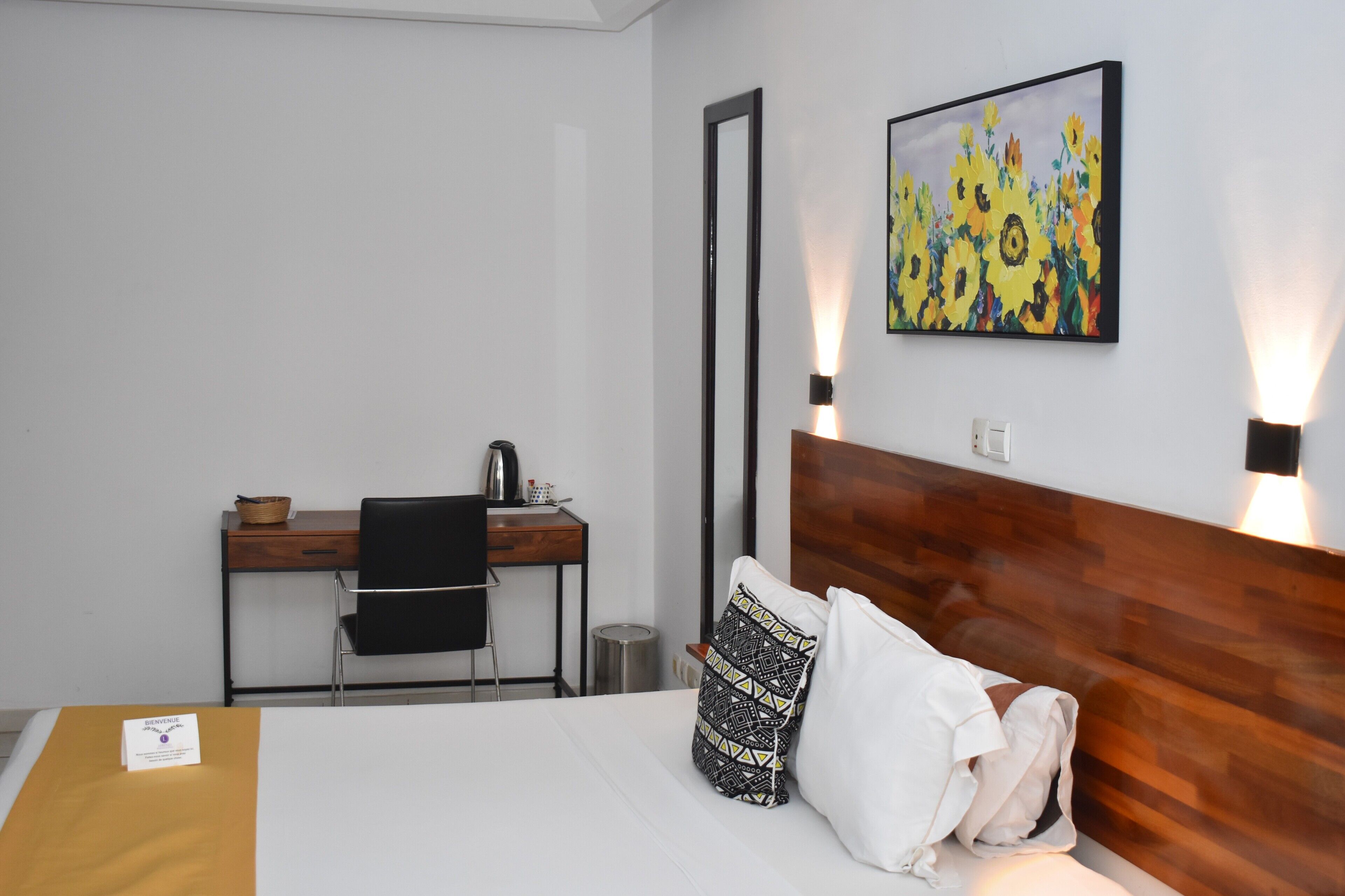 A hotel room with a bed, a desk, a chair, a trash bin, and a painting on the wall.