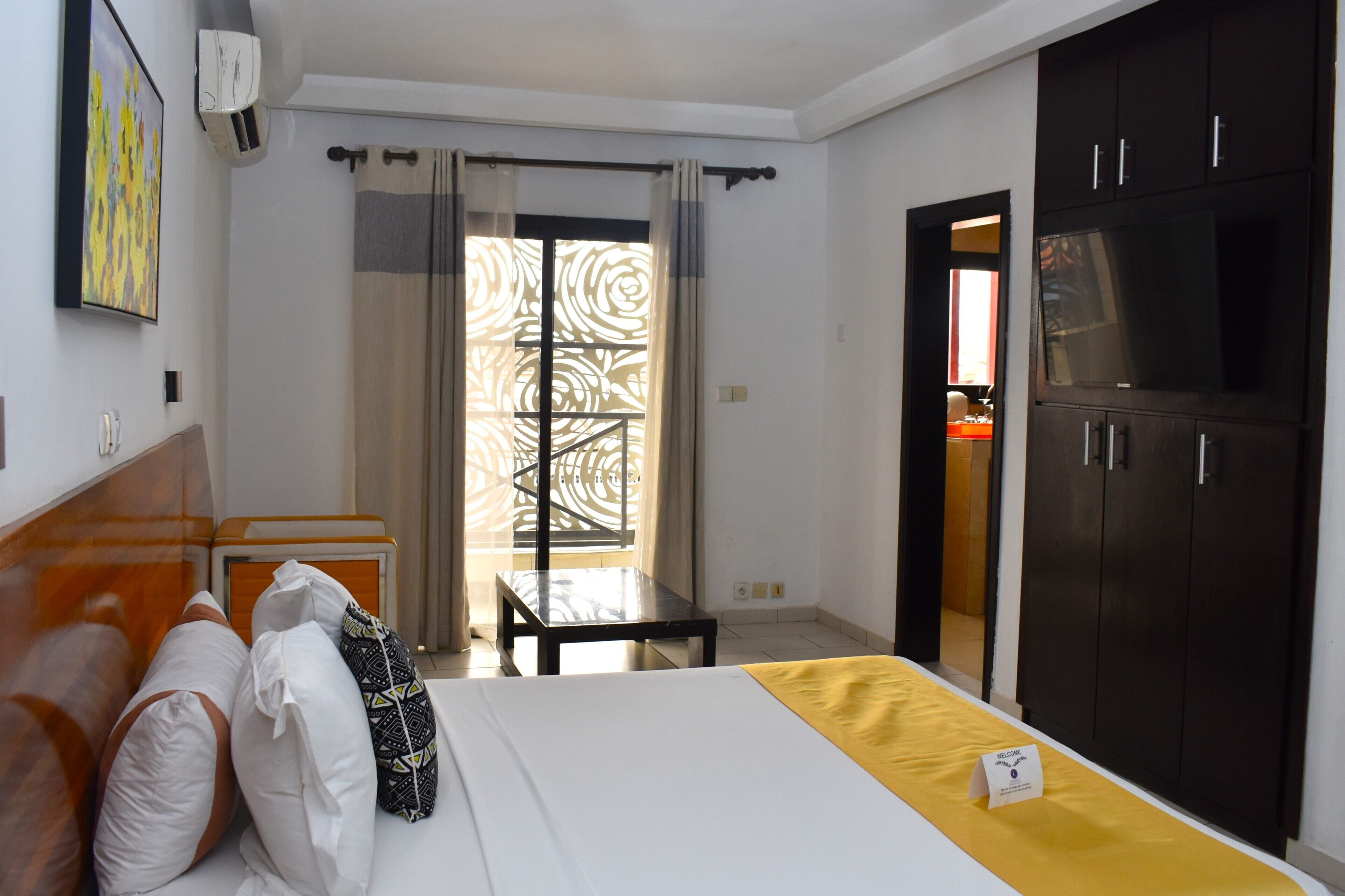 A hotel room with a bed, a desk, a wardrobe, and a view through a window with curtains.