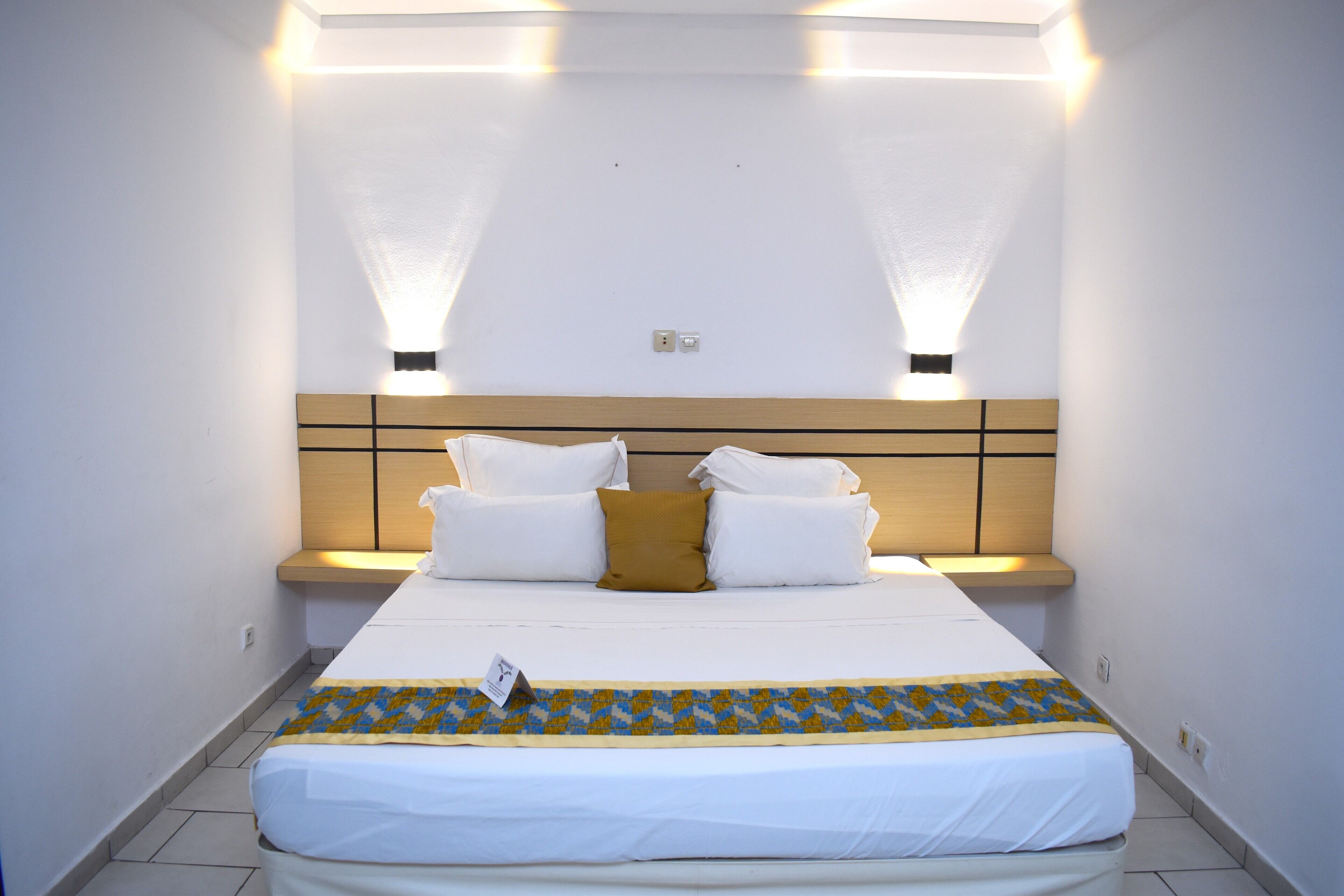 A hotel room with a large bed, bedside tables, and wall-mounted lighting.
