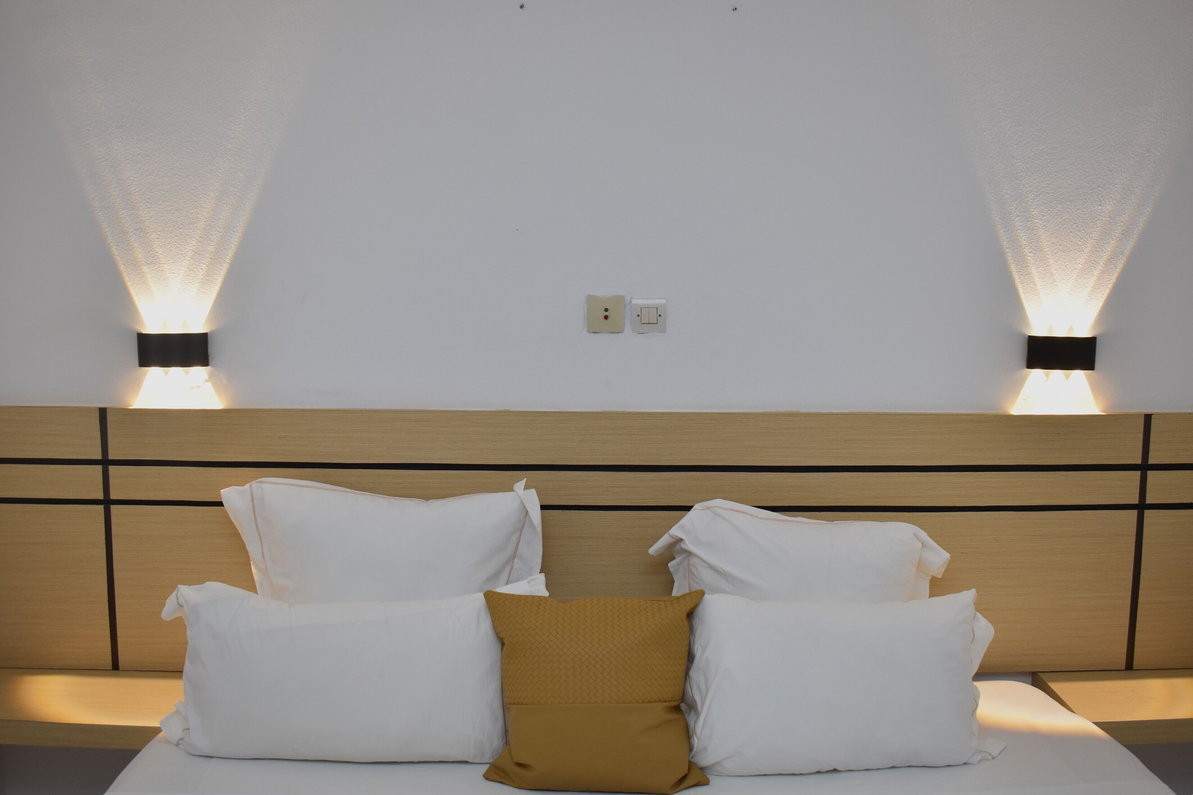 A hotel room with a wooden headboard, two wall-mounted lights, and a bed with white and mustard pillows.