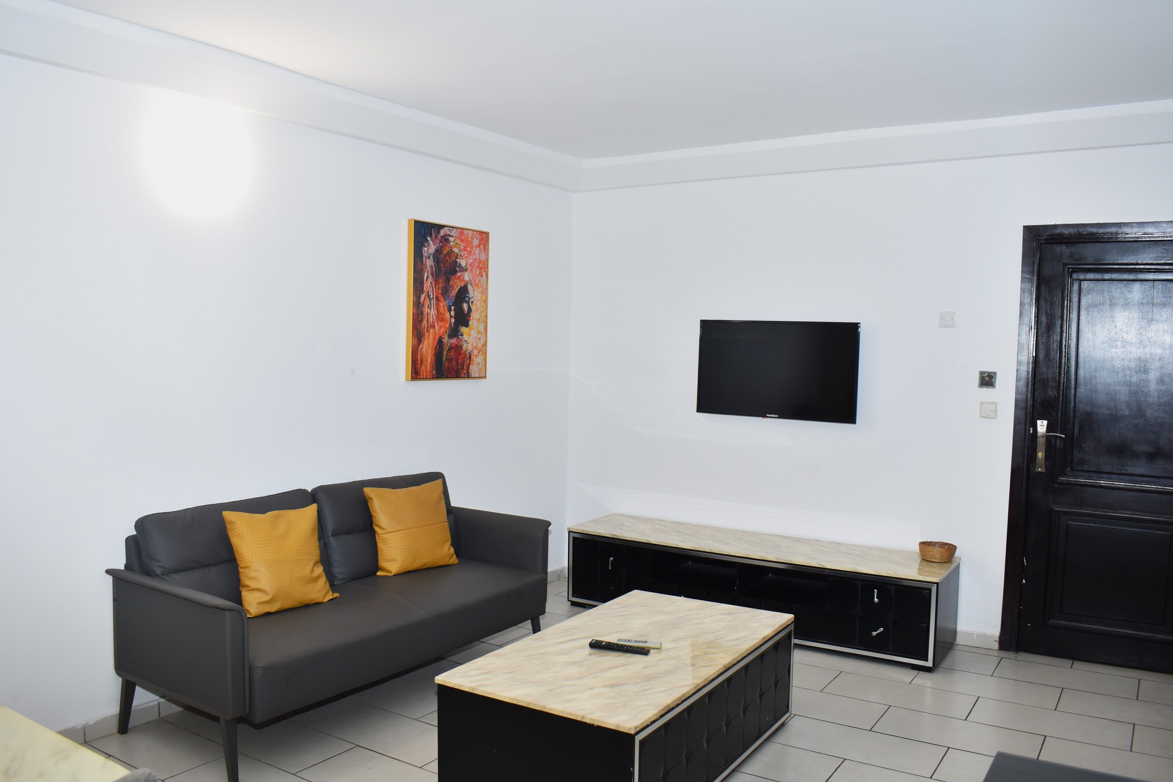A modern living room with a black sofa, a wooden coffee table, a flat-screen TV mounted on the wall, and a black door.
