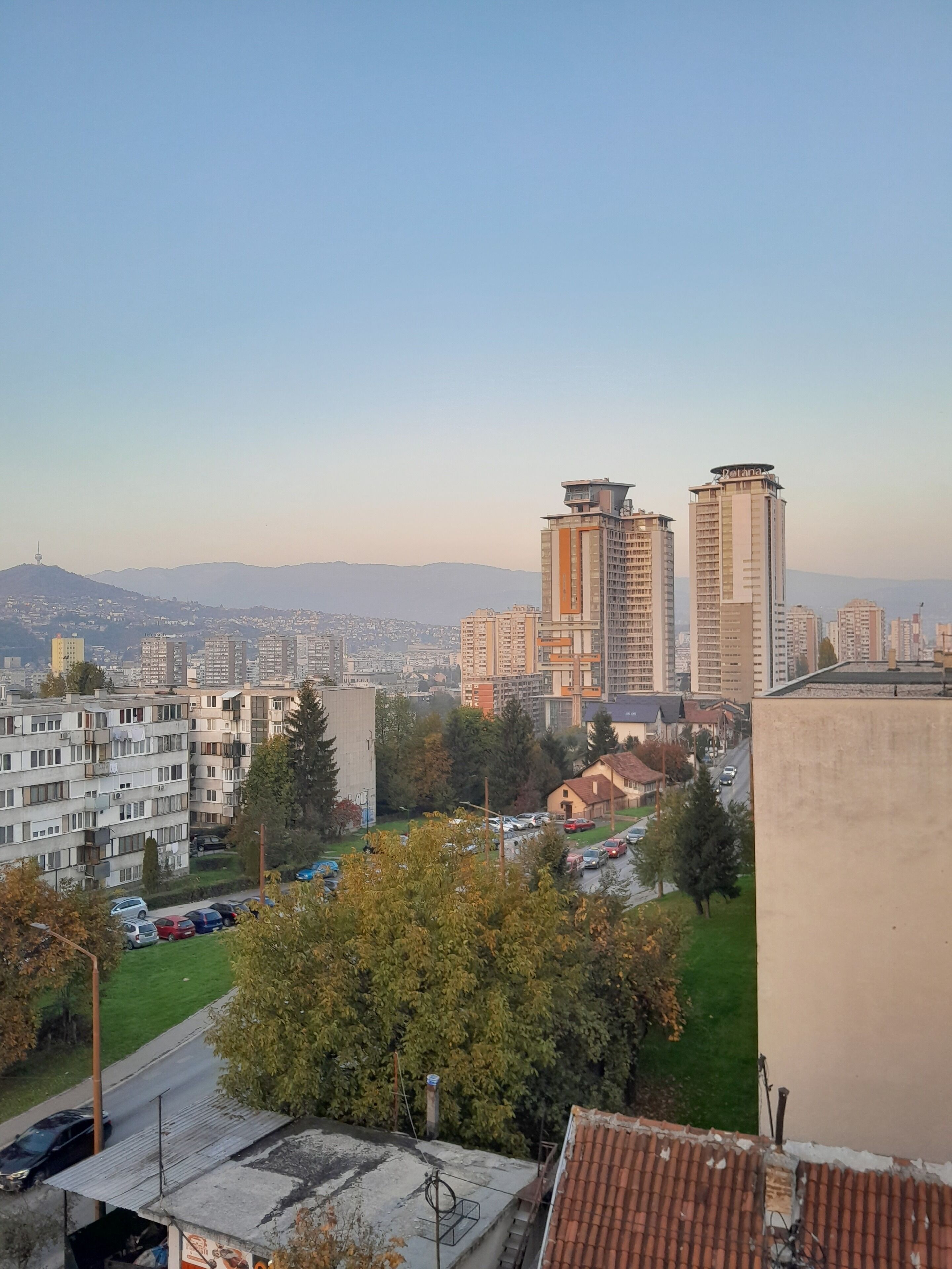 A cityscape with high-rise buildings, a clear sky, and a distant mountain range.