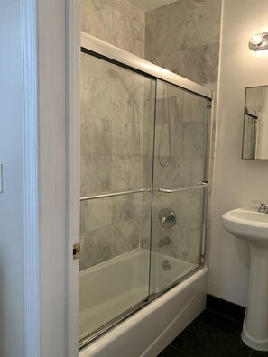 Un baño con ducha de vidrio, lavamanos blanco y pared con azulejos de mármol.