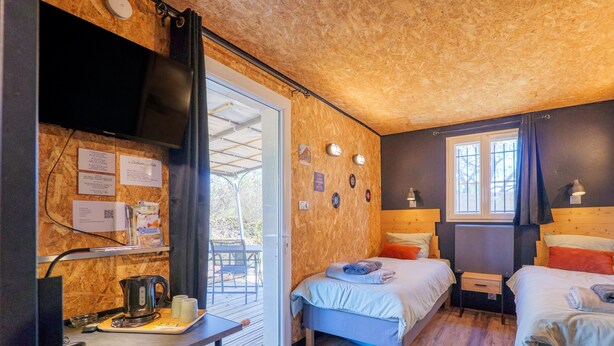 Una habitación con dos camas, un escritorio con hervidor, televisión y una ventana con cortinas.