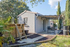 Un pequeño patio al aire libre con un suelo de madera, una pérgola, un cobertizo pequeño y un espacio de estar con sillas y una mesa.