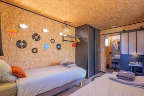 Una habitación con dos camas, una pared de madera con discos de vinilo, un espejo y un baño pequeño.
