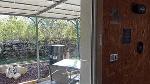 Un espacio al aire libre cubierto con una mesa, sillas, un contenedor de basura y un muro de piedra.