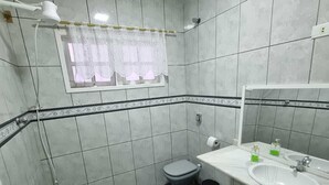 Een badkamer met witte betegelde wanden, een zwarte vloer, een toilet, een wastafel met spiegel en een raam met kantgordijnen.