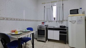 Een kleine keuken met een eettafel, stoelen, een gasfornuis, een magnetron en een koelkast.