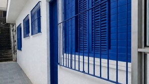 Een gebouw met een witte gevel, blauwe luiken en een metalen hek.