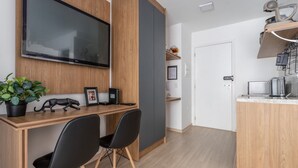 A modern kitchen with a built-in oven, a microwave, and a sink. There is a wooden dining table with two chairs and a potted plant. - Studio in Liberdade 270m From Metro Mol0502 (São Paulo)