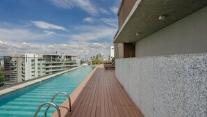 A rooftop swimming pool with a wooden deck, a concrete wall, and a view of surrounding buildings. - Your Urban Retreat Near the Subway - Iby1613 (São Paulo)