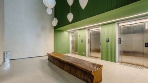 Un área de ascensor moderna con paredes verdes, un banco de madera y dos ascensores.