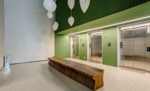 Et moderne elevatormiljø med grønne vægge, en træbænk og to elevatorer.