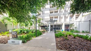 L’entrée d’un hôtel, avec une enseigne indiquant « HOUX 551 », et une galerie couverte menant au bâtiment.