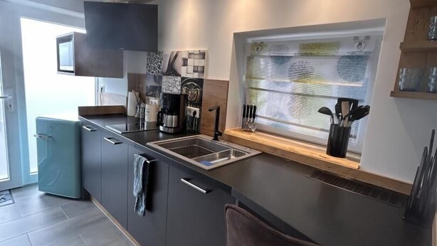 A modern kitchen with dark cabinets, a black countertop, and a window with a view. - NEW! Apartment Engel (Weilburg)