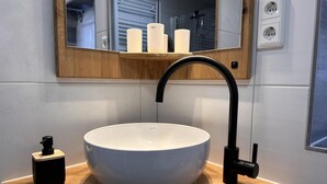 A bathroom with a white vessel sink, a black faucet, a wooden vanity, and a mirror above the sink. - NEW! Apartment Engel (Weilburg)