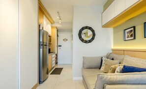 A modern living room with a sofa, a wall clock, and a kitchen area with a refrigerator. - Complete Stay With Pool and gym Steps From the Metro in Pinheiros - SP - LOF (São Paulo)