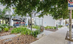 A modern building with a sign for 'HOUX' and a 'sedzone' logo, surrounded by greenery and a paved sidewalk. - Complete Stay With Pool and gym Steps From the Metro in Pinheiros - SP - LOF (São Paulo)