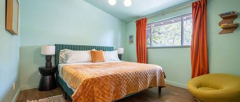 Un dormitorio con una cama, una mesita de noche, una silla, un ventanal con cortinas y una lámpara en el techo.