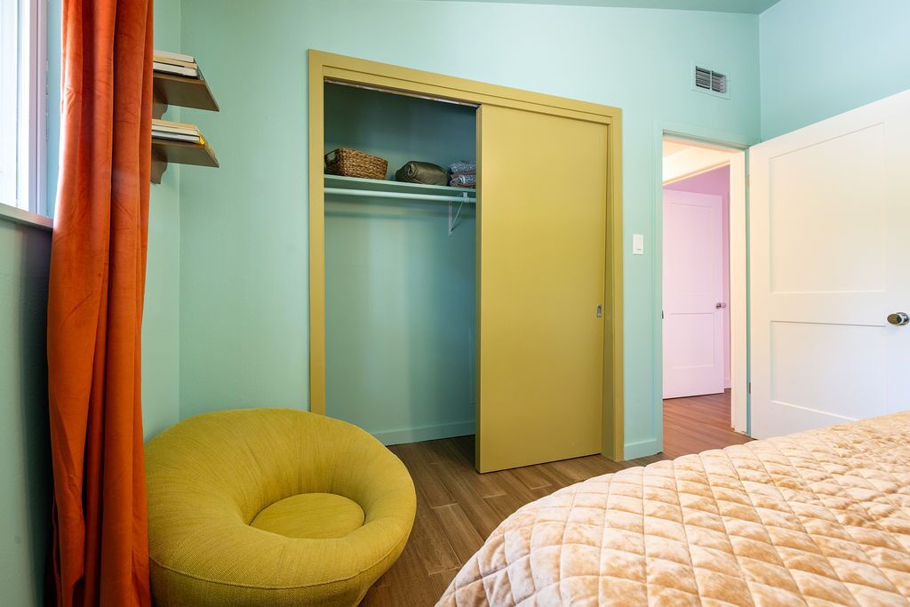 Une chambre à coucher avec un lit, une chaise jaune, une armoire et une porte donnant sur une autre pièce.
